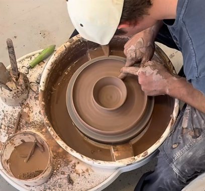Lucas at the wheel, hands covered in clay, centering a form in a studio splash pan